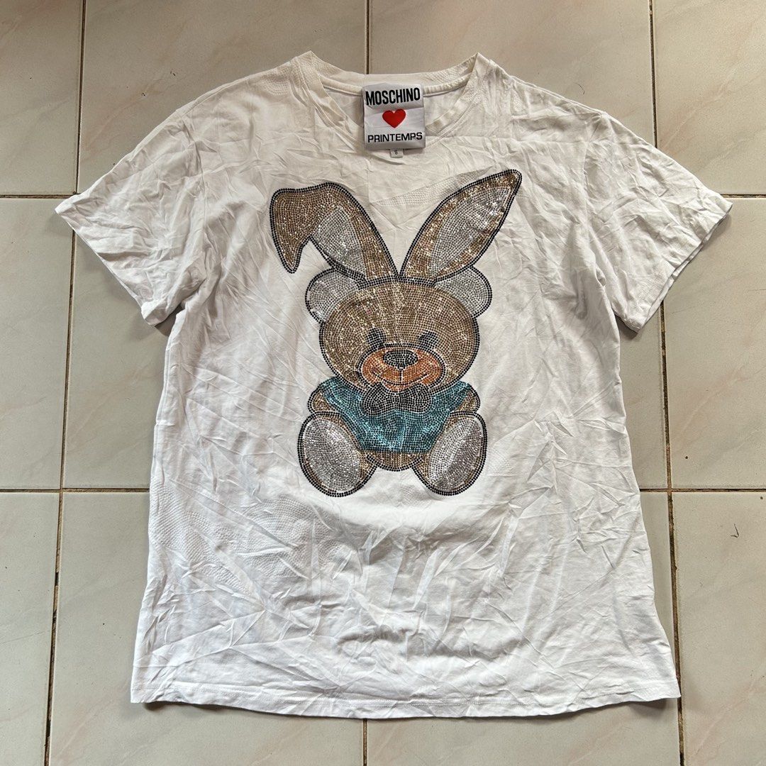 Moschino Printemps Rhinestone Bunny 🔥 (Category: Shirts) located in Jinoba-an. Submitted by eegiboy (Listing ID 1467024722, Image 1). Description: - Brand: Moschino Printemps - Color: White - Material: 100% Cotton - Size: S (tag attached) - Design: Sparkly rhinestone bunny bear graphic on front, classic crew neck, short sleeves - Features: Special collaboration inner neck label, fun statement piece - Care: Dry clean only in mesh bag Wts: Moschin