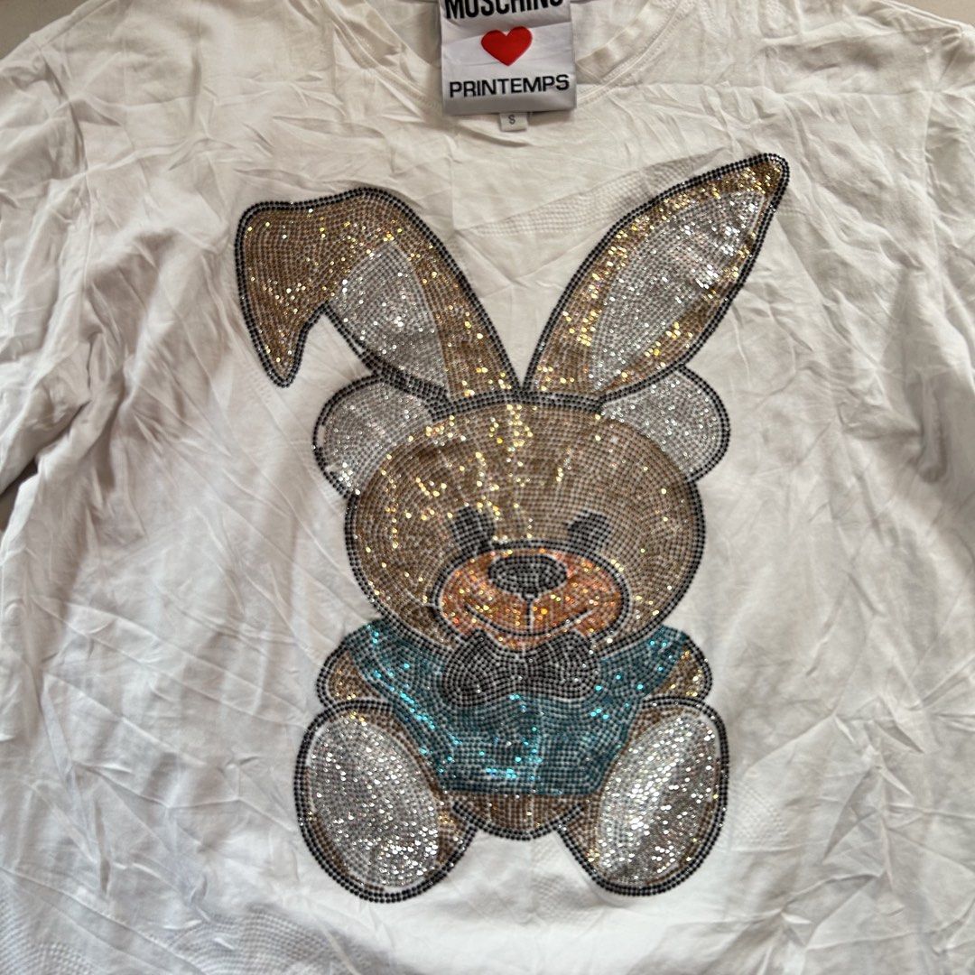 Moschino Printemps Rhinestone Bunny 🔥 (Category: Shirts) located in Jinoba-an. Submitted by eegiboy (Listing ID 1467024722, Image 3). Description: - Brand: Moschino Printemps - Color: White - Material: 100% Cotton - Size: S (tag attached) - Design: Sparkly rhinestone bunny bear graphic on front, classic crew neck, short sleeves - Features: Special collaboration inner neck label, fun statement piece - Care: Dry clean only in mesh bag Wts: Moschin