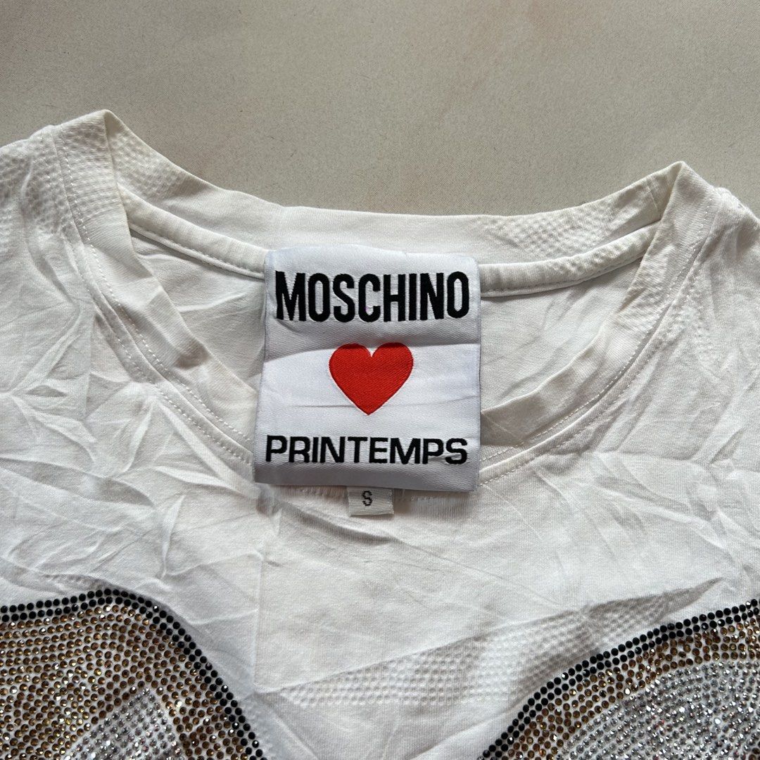 Moschino Printemps Rhinestone Bunny 🔥 (Category: Shirts) located in Jinoba-an. Submitted by eegiboy (Listing ID 1467024722, Image 2). Description: - Brand: Moschino Printemps - Color: White - Material: 100% Cotton - Size: S (tag attached) - Design: Sparkly rhinestone bunny bear graphic on front, classic crew neck, short sleeves - Features: Special collaboration inner neck label, fun statement piece - Care: Dry clean only in mesh bag Wts: Moschin
