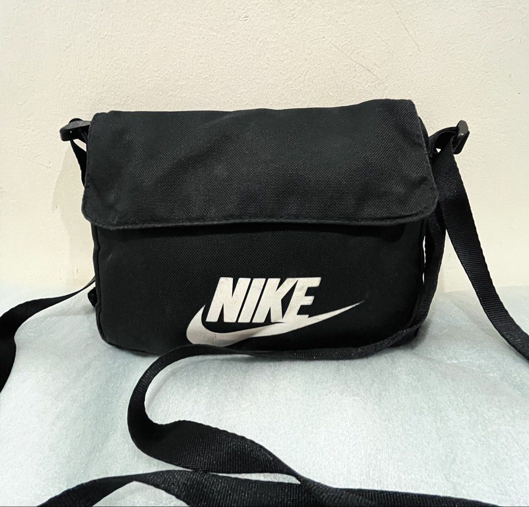 Nike Black Messenger Crossbody Bag (Category: Sling Bags) located in Talisay. Submitted by cherylu (Listing ID 1466975938, Image 1). Description: Black canvas messenger bag from Nike. Large white logo on the front flap. Adjustable shoulder strap. Inside has a zippered mesh pocket with a small Nike tag. Main compartment holds daily essentials. Clean fabric inside and out..