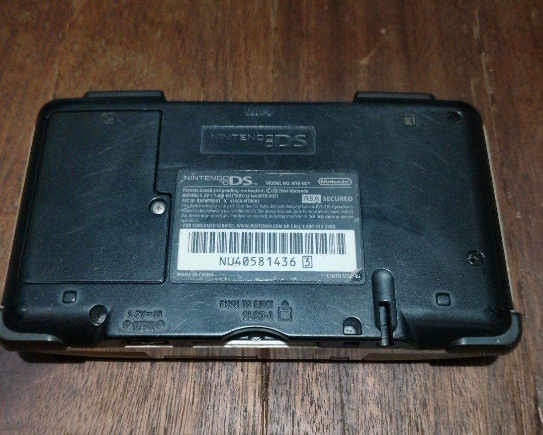 Nintendo Ds phat (Category: Nintendo) located in Manila. Submitted by boyhet.thrift15 (Listing ID 1467111462, Image 2). Description: Original Nintendo DS handheld console in silver. Model NTR-001. Dual screen setup with D-pad and action buttons. Visible scratches and wear on the outer casing and screens. Hinge shows some discoloration. Battery cover is attached on the back. Powers up DS games using Slot 1. Retro gaming system for classic titles. 