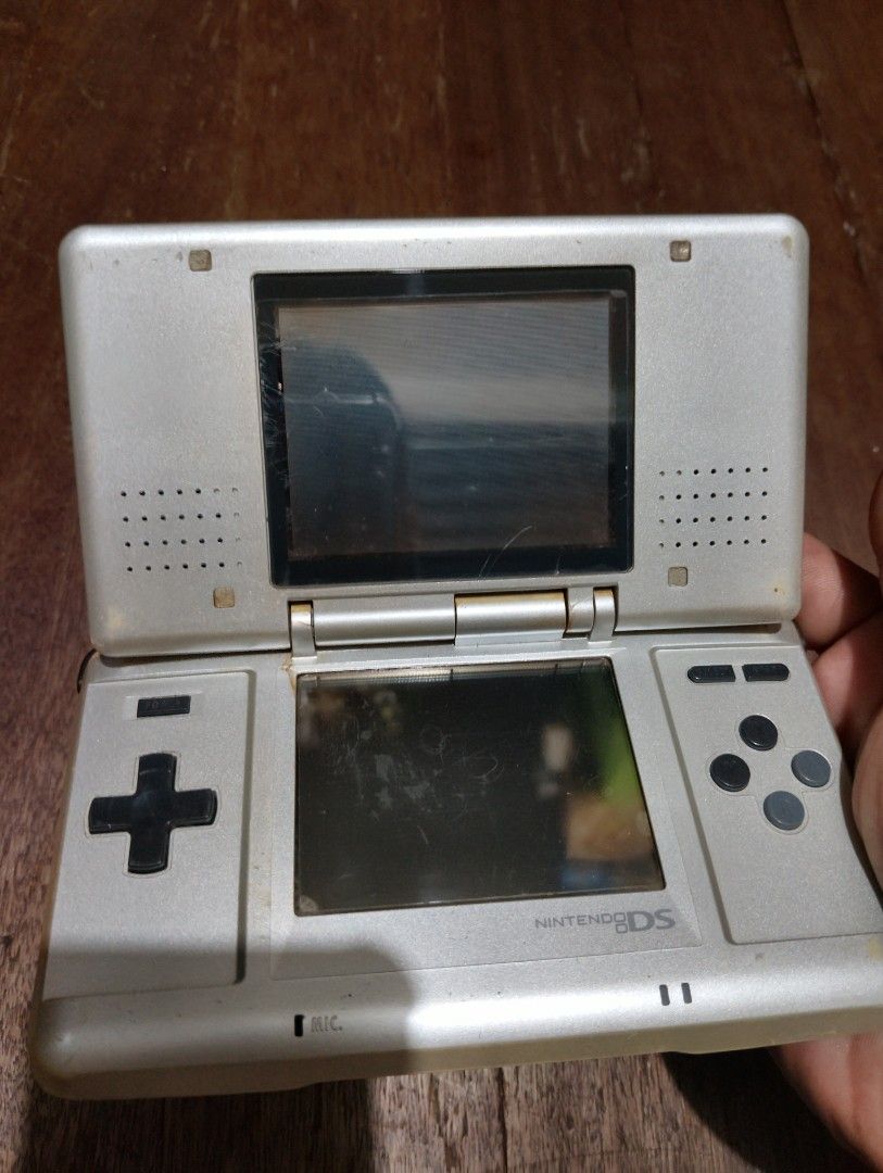 Nintendo Ds phat (Category: Nintendo) located in Manila. Submitted by boyhet.thrift15 (Listing ID 1467111462, Image 3). Description: Original Nintendo DS handheld console in silver. Model NTR-001. Dual screen setup with D-pad and action buttons. Visible scratches and wear on the outer casing and screens. Hinge shows some discoloration. Battery cover is attached on the back. Powers up DS games using Slot 1. Retro gaming system for classic titles. 