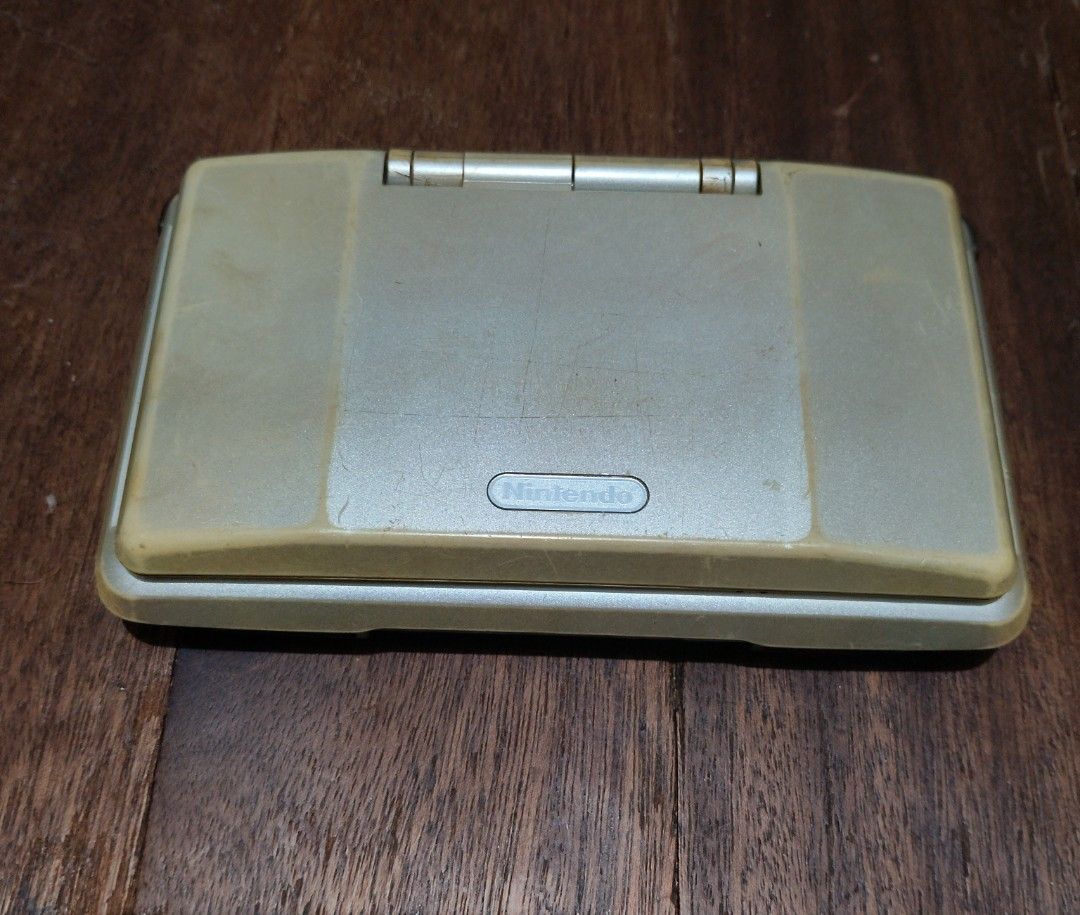 Nintendo Ds phat (Category: Nintendo) located in Manila. Submitted by boyhet.thrift15 (Listing ID 1467111462, Image 1). Description: Original Nintendo DS handheld console in silver. Model NTR-001. Dual screen setup with D-pad and action buttons. Visible scratches and wear on the outer casing and screens. Hinge shows some discoloration. Battery cover is attached on the back. Powers up DS games using Slot 1. Retro gaming system for classic titles. 