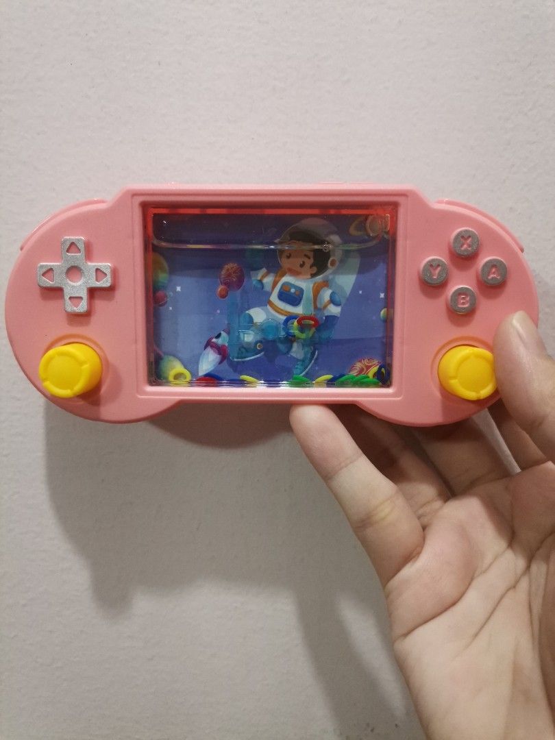 Pink Astronaut Handheld Water Game Toy (Category: Kids Toys) located in Makati City. Submitted by kookybearsstuff (Listing ID 1467088943, Image 1). Description: - Adorable pink astronaut and space-themed design - Shaped like a retro video game console with a d-pad, buttons, and two yellow control knobs - Clear water chamber filled with fun, colorful floating rings - Great nostalgic puzzle game for kids or toy collectors.