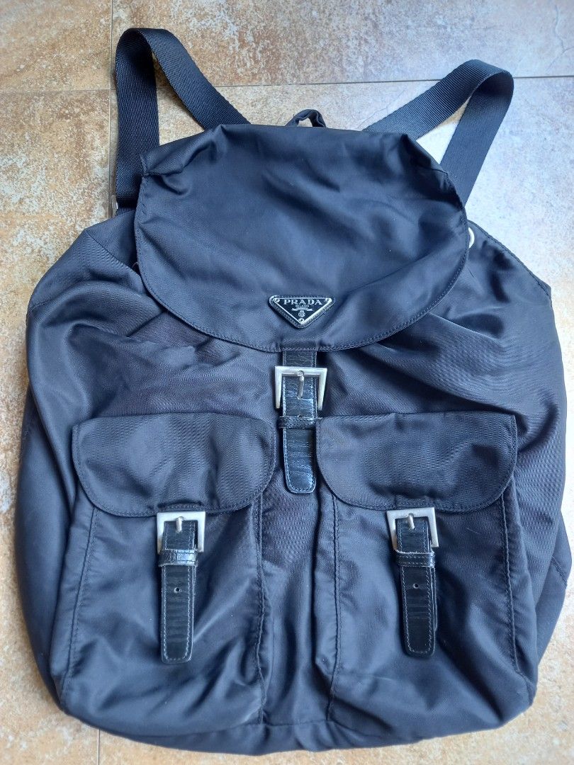 Prada Black Nylon Backpack with Leather Straps and Buckles (Category: Backpacks) located in Davao. Submitted by kirk214red-50020 (Listing ID 1466982797, Image 1). Description: - Brand: Prada - Material: Durable black nylon with leather trim - Hardware: Silver-tone with engraved Prada lettering - Closure: Drawstring top and front flap with buckled strap - Pockets: Two front pockets with secure buckle closures - Straps: Adjustable fabric shoulder s