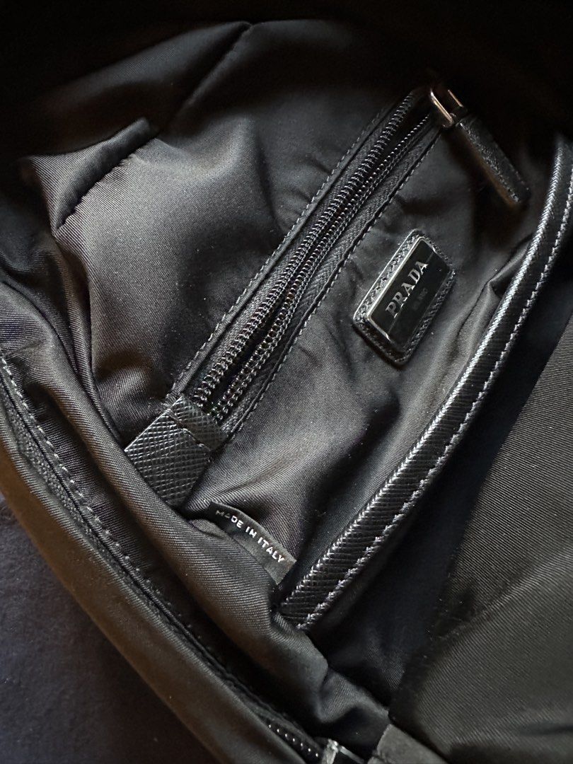 Prada Black Nylon Sling Backpack (Category: Backpacks) located in San Juan City. Submitted by travellingpete (Listing ID 1467044667, Image 3). Description: - Authentic Prada sling backpack in durable black nylon - Silver-tone hardware with branded buckles and side release clasp - Features iconic triangular enamel logo plaque on the front - Main compartment includes a secure zip pocket and 'Made in Italy' fabric tag - Comfortable, adjustable mesh-