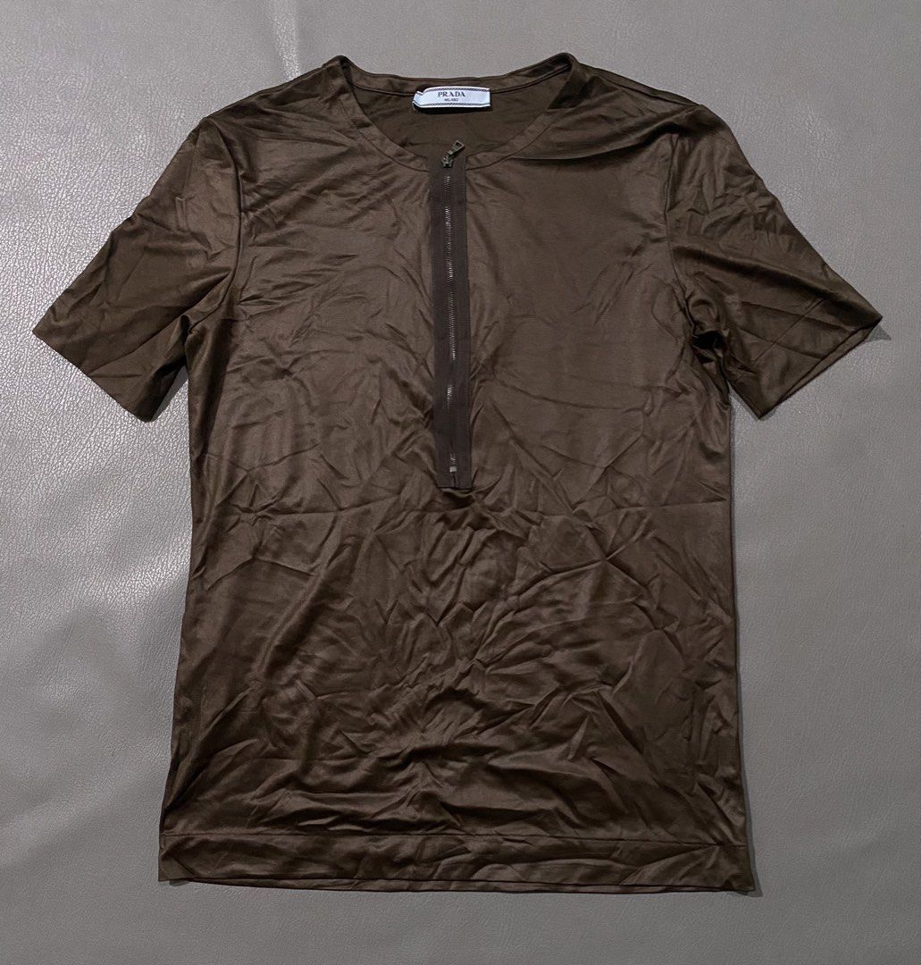 Prada Brown Jersey Zip Front Short Sleeve Top (Category: Tshirts & Polo Shirts ) located in Pozorrubio. Submitted by izaykite2g (Listing ID 1467113192, Image 1). Description: - Prada Brown Jersey Zip Front Short Sleeve Top - Color: Brown - Size: Medium (M) - 17 inches width - 25 inches length - Material: 100% polyester with a smooth, slightly lustrous finish - Design: Short sleeve, round neckline, regular fit silhouette - Closure: Half-zip front 