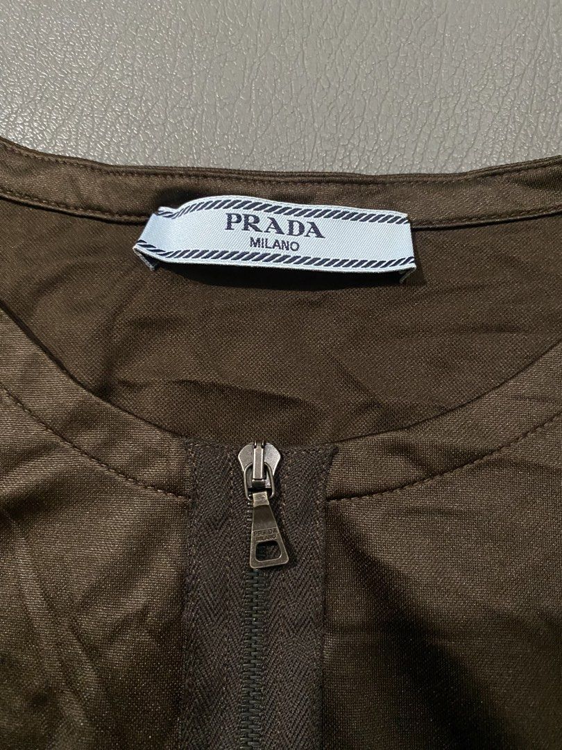 Prada Brown Jersey Zip Front Short Sleeve Top (Category: Tshirts & Polo Shirts ) located in Pozorrubio. Submitted by izaykite2g (Listing ID 1467113192, Image 2). Description: - Prada Brown Jersey Zip Front Short Sleeve Top - Color: Brown - Size: Medium (M) - 17 inches width - 25 inches length - Material: 100% polyester with a smooth, slightly lustrous finish - Design: Short sleeve, round neckline, regular fit silhouette - Closure: Half-zip front 