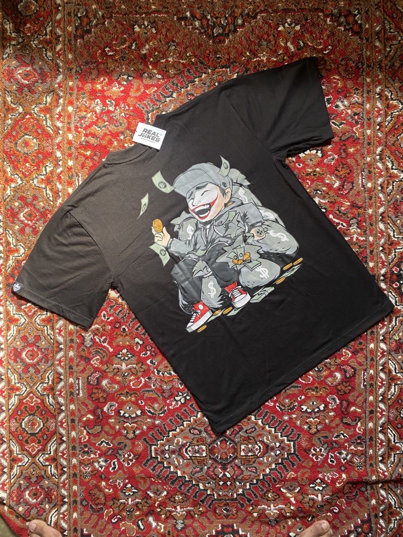 Real Jokes Black Graphic Tee (Category: Shirts) located in Manila. Submitted by nastorjeri57541 (Listing ID 1467125688, Image 2). Description: - Brand: Real Jokes - Condition: Brand new with tag, unused - Color: Black - Design: Large cartoon character surrounded by money and cash on the back, small circular logo on the front chest - Fit: Short sleeves, standard crew neck - Size: Large.