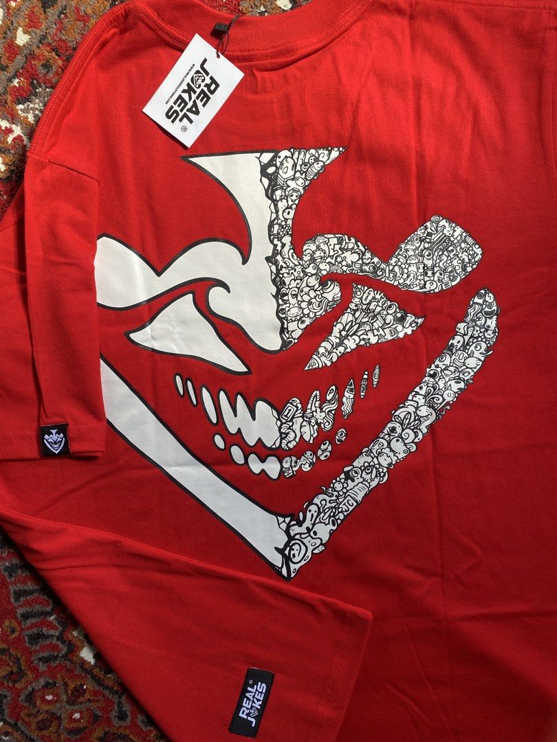 Real Jokes Red Graphic Tee Size L (Category: Tshirts & Polo Shirts ) located in Manila. Submitted by nastorjeri57541 (Listing ID 1467124965, Image 3). Description: - Brand: Real Jokes - Condition: Brand new with tags attached - Size: L - Color: Red - Front Design: Bold white 'REAL JOKES' text graphic with a quirky joker face - Back Design: Large abstract doodle graphic print - Details: Small woven logo label on the left sleeve hem.