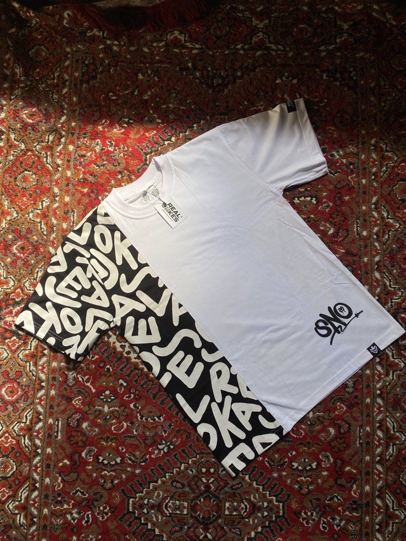Real Jokes Split Design Typography T-Shirt (Category: Shirts) located in Manila. Submitted by nastorjeri57541 (Listing ID 1467125562, Image 1). Description: - Brand: Real Jokes - Condition: Brand new, never worn, with original tags attached - Design: Unique split design (white on one side, black with bold typography on the other) - Details: Short sleeves, crew neck, graphic print near the bottom hem, small brand tags on sleeve cuff and hem - Perf