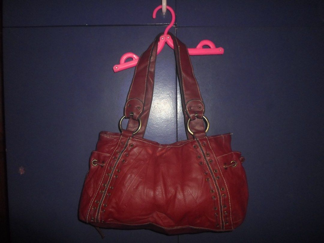 Red leather shoulder bag with grommet details and side drawstrings (Category: Shoulder Bags) located in Manila. Submitted by macinasley96164 (Listing ID 1467152963, Image 1). Description: - Color/Material: Deep red textured faux leather - Hardware: Brass-toned metal rings and front grommets - Design: Vertical front panels with contrast stitching and side drawstrings with knotted ends - Interior: Spacious main compartment for your daily essentials