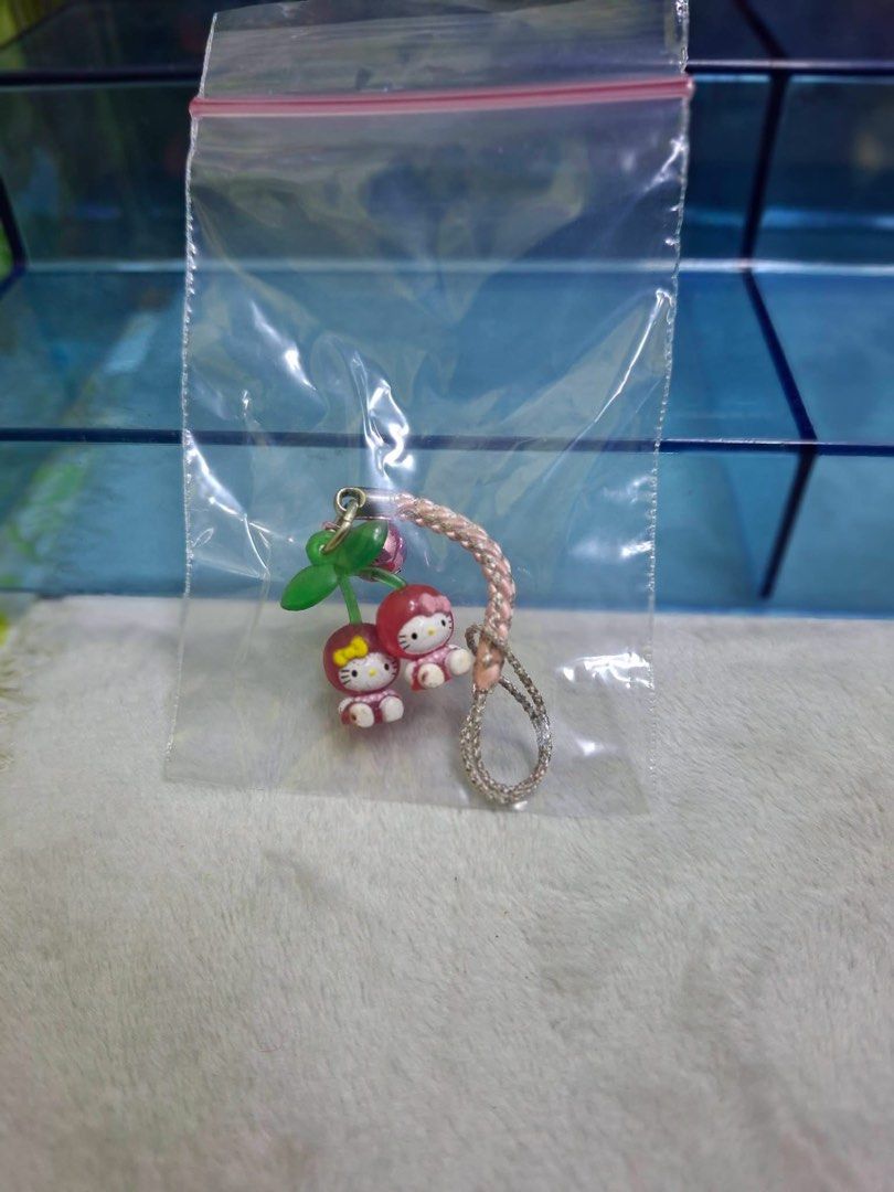 Sanrio Hello Kitty Cherry Strap Charm (Category: Charms) located in Manila. Submitted by janetecson05 (Listing ID 1467061046, Image 1). Description: - Authentic Sanrio phone charm featuring Kitty dressed as adorable cherries - Detailed with a green stem and a small working pink bell - Comes with a durable pink braided strap for easy attachment.