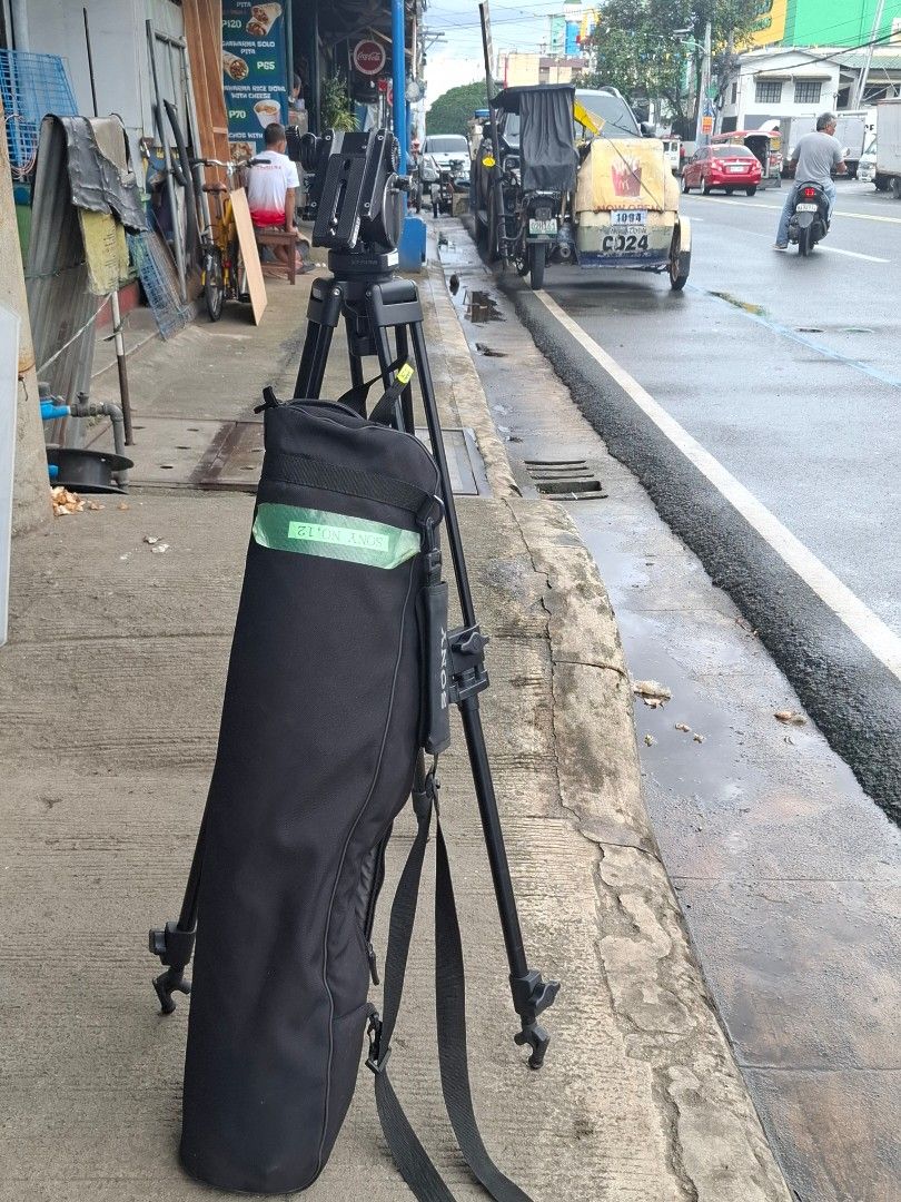Sony VCT-PG11RMB Professional Video Tripod (Category: Tripods & Monopods) located in Manila. Submitted by rocksolid227 (Listing ID 1467023418, Image 2). Description: Sony VCT-PG11RMB tripod setup. Pan head with adjustable handle included. Sturdy aluminum build with dual leg design for extra stability. Mid-level spreader keeps legs locked in place. Carrying bag included with Sony labeling and tape ID mark. Note the broken plastic piece on one of t