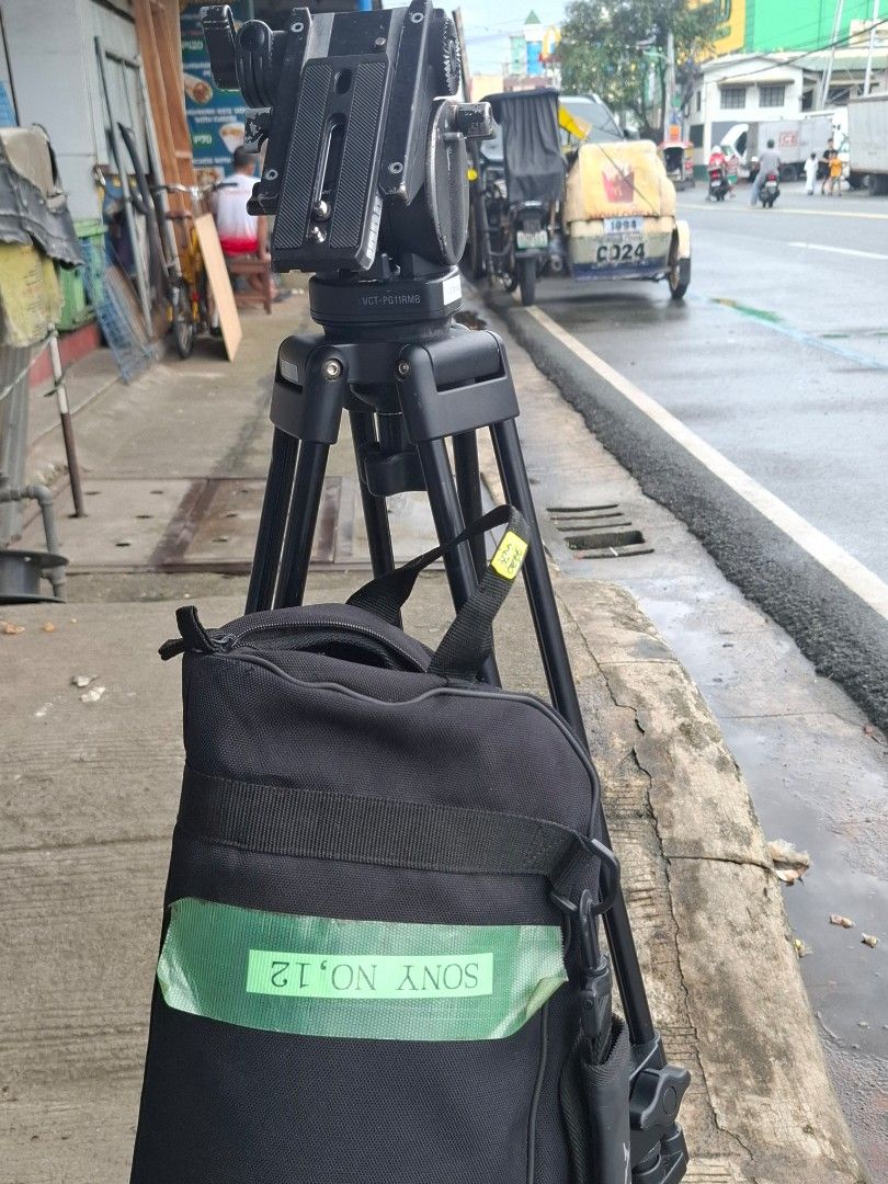 Sony VCT-PG11RMB Professional Video Tripod (Category: Tripods & Monopods) located in Manila. Submitted by rocksolid227 (Listing ID 1467023418, Image 3). Description: Sony VCT-PG11RMB tripod setup. Pan head with adjustable handle included. Sturdy aluminum build with dual leg design for extra stability. Mid-level spreader keeps legs locked in place. Carrying bag included with Sony labeling and tape ID mark. Note the broken plastic piece on one of t