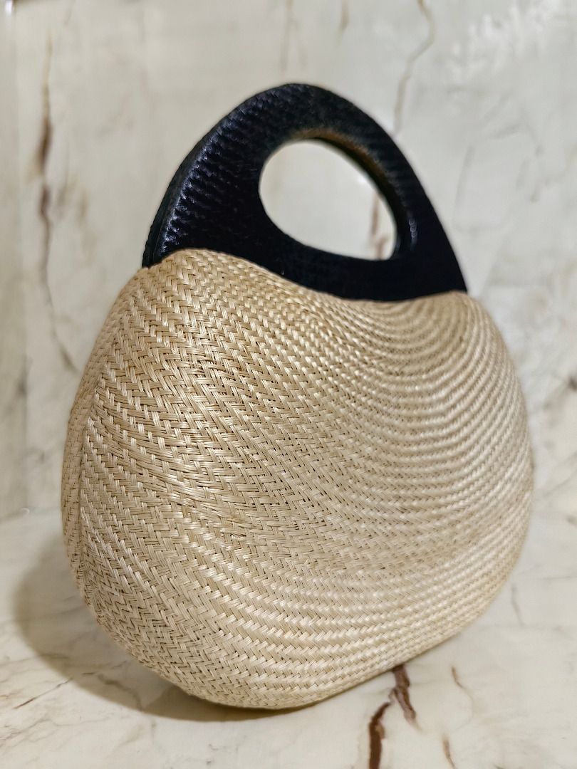 Straw Woven Handbag with Grey Structured Top Handle (Category: Beach Bags) located in Tarlac. Submitted by jeremiah.curator.2026 (Listing ID 1467112006, Image 3). Description: - Natural straw woven body with a trendy curved shape - Stylish dark grey structured top handle - Flat oval base designed to stand firmly on surfaces - Compact handheld size for effortless carrying - Ideal accessory for daytime outings or beach trips.