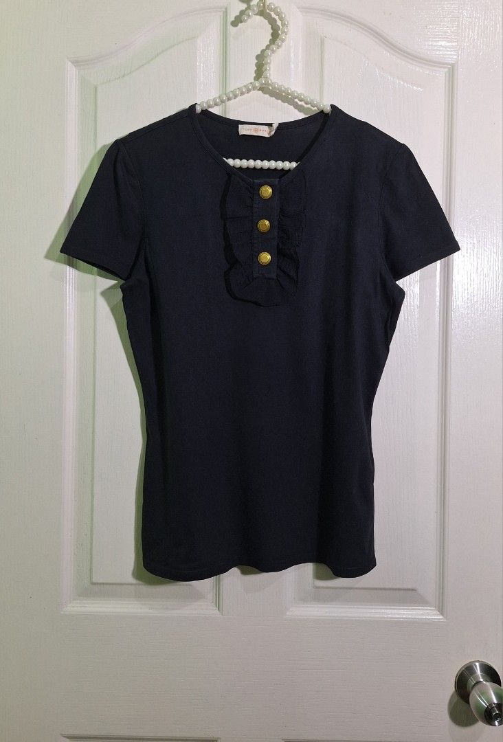 Tory Burch Black Ruffle Gold Button Tee small - medium (Category: Shirts) located in San Pablo. Submitted by allyourbrandedneeds (Listing ID 1467018537, Image 2). Description: - Brand: Tory Burch - Color: Classic Black - Size: Small - Material: Soft, breathable cotton - Design: Round neckline, ruffled front placket, and 3 gold-tone embossed logo buttons - Origin: Made in India - Condition: Clean inside labels with global care info attached.