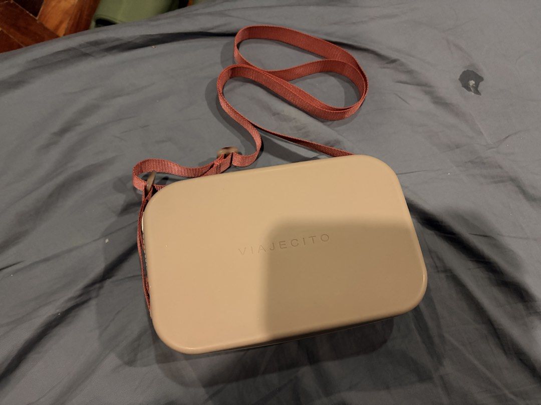 Viajecito Silicone Crossbody Bag (Category: Cross-body Bags) located in Marikina City. Submitted by nj1989 (Listing ID 1467120504, Image 1). Description: - Brand/Model: Viajecito Crossbody Bag Flaw: Discoloration on the lining inside of the bag - Color: Taupe body with a dusty pink strap - Material: Structured, water-resistant hard-shell silicone - Closure: Smooth all-around zipper - Strap: Adjustable woven strap with side loops - Details: Minima