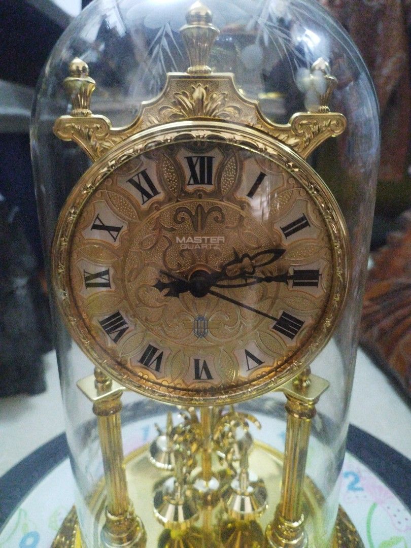 vintage anniversary glass dome clock (Category: Vintage Collectibles) located in San Rafael. Submitted by jflshoppe1989 (Listing ID 1467035202, Image 3). Description: height 13 inches lenght 8 inches Key Features Glass Dome: A blown or molded clear glass cloche (often etched with floral motifs) protecting the delicate mechanism inside. Dial & Numerals: An ornate, embossed golden face featuring Roman numerals and decorative filigree center pattern