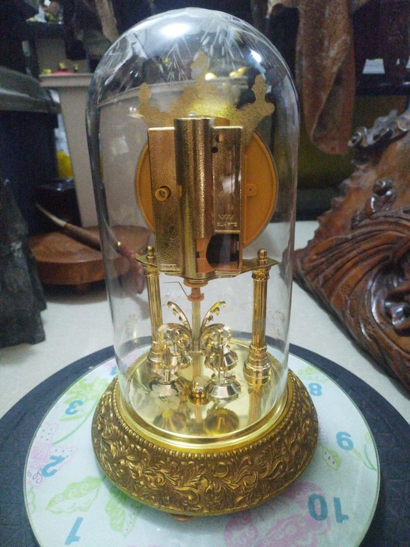vintage anniversary glass dome clock (Category: Vintage Collectibles) located in San Rafael. Submitted by jflshoppe1989 (Listing ID 1467035202, Image 2). Description: height 13 inches lenght 8 inches Key Features Glass Dome: A blown or molded clear glass cloche (often etched with floral motifs) protecting the delicate mechanism inside. Dial & Numerals: An ornate, embossed golden face featuring Roman numerals and decorative filigree center pattern