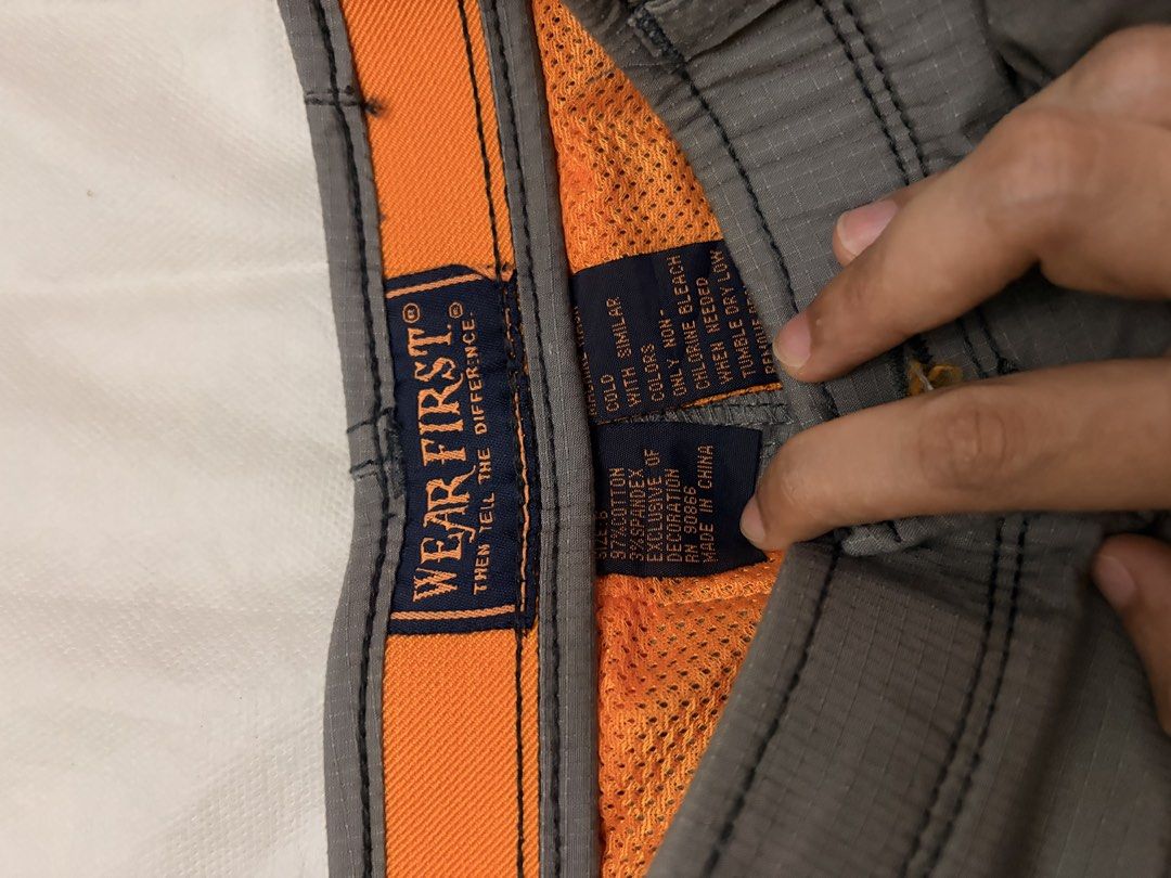Wear First Cargo Shorts Grey Size 8 (Category: Shorts) located in Dasmarinas. Submitted by thriftcavite (Listing ID 1466986579, Image 2). Description: - Brand: Wear First - Size: Tagged Size 8 - Color: Grey with bright orange interior waistband lining - Material: 97% cotton, 3% spandex blend (slight stretch) - Storage: Multiple utility pockets with secure button and zipper details - Care: Machine washable - Condition: Durable everyday shorts, per
