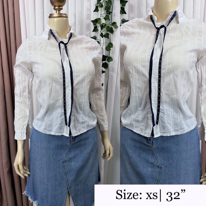 White Blouse Size XS (Category: Blouses) located in Manila. Submitted by escherichiaa (Listing ID 1467137483, Image 1). Description: White long sleeve button-up shirt with vertical stripe texture. Attached dark ribbon tie at the collar. Fitted cut, classic collar design. Lightweight material, easy to style for work or casual days. Tag says Always Lucky with Chinese characters..