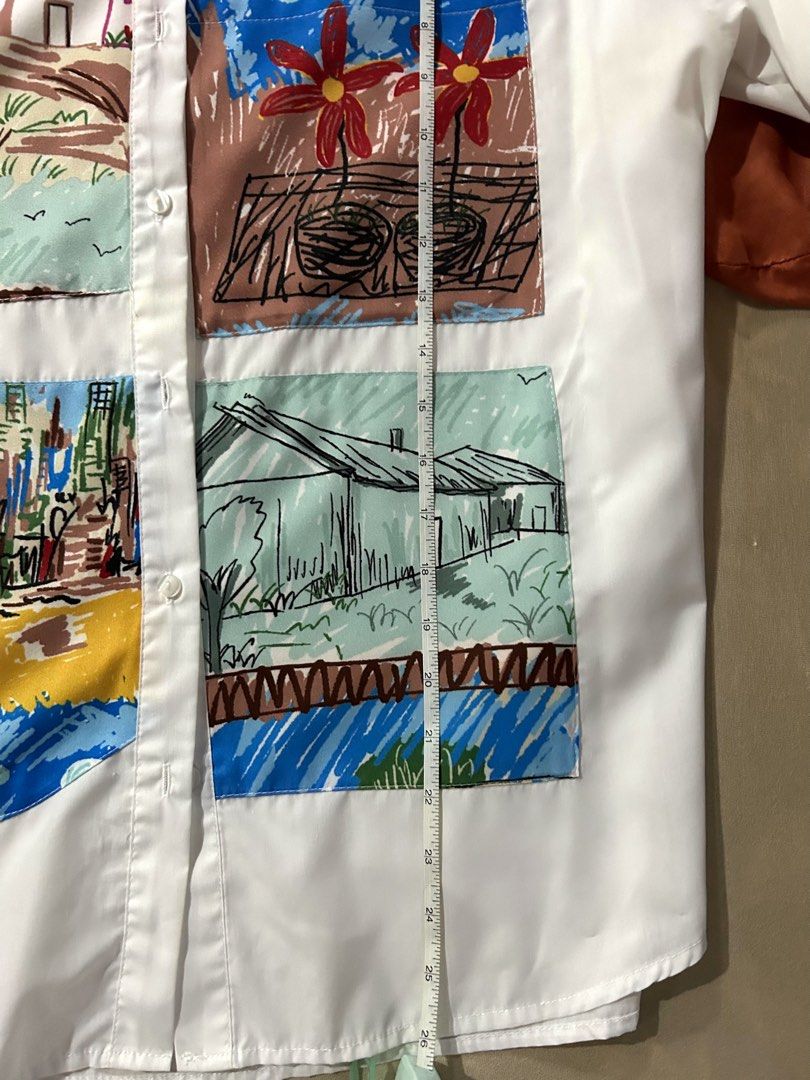 White Button-Up Shirt With Artistic Patchwork Prints (Category: Shirts) located in Cainta. Submitted by unboxingstuff (Listing ID 1467020266, Image 3). Description: - Color: Crisp white with vibrant, multi-colored illustrated patch pockets - Design: Features bright landscape and cityscape drawings in blue, red, green, and yellow - Details: Classic collar, long sleeves, and front button-down closure - Material: Smooth, lightweight, and comfortable