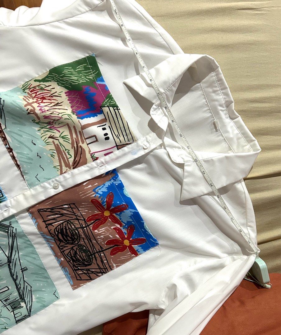 White Button-Up Shirt With Artistic Patchwork Prints (Category: Shirts) located in Cainta. Submitted by unboxingstuff (Listing ID 1467020266, Image 2). Description: - Color: Crisp white with vibrant, multi-colored illustrated patch pockets - Design: Features bright landscape and cityscape drawings in blue, red, green, and yellow - Details: Classic collar, long sleeves, and front button-down closure - Material: Smooth, lightweight, and comfortable
