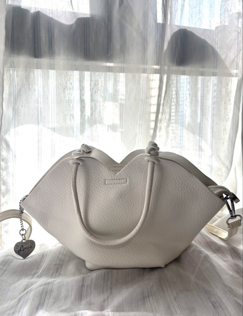 White PU Leather Tote Bag with Shoulder Strap (Category: Tote Bags) located in Makati City. Submitted by bittersweet818ta (Listing ID 1467135827, Image 1). Description: White faux leather handbag with unique petal-shaped top edge. Dual top handles plus an adjustable, detachable long shoulder strap. Includes a cute 'Love' heart charm hanging from the side zip. Main zip closure keeps items secure. Textured finish all over. Clean inside and out. Gre