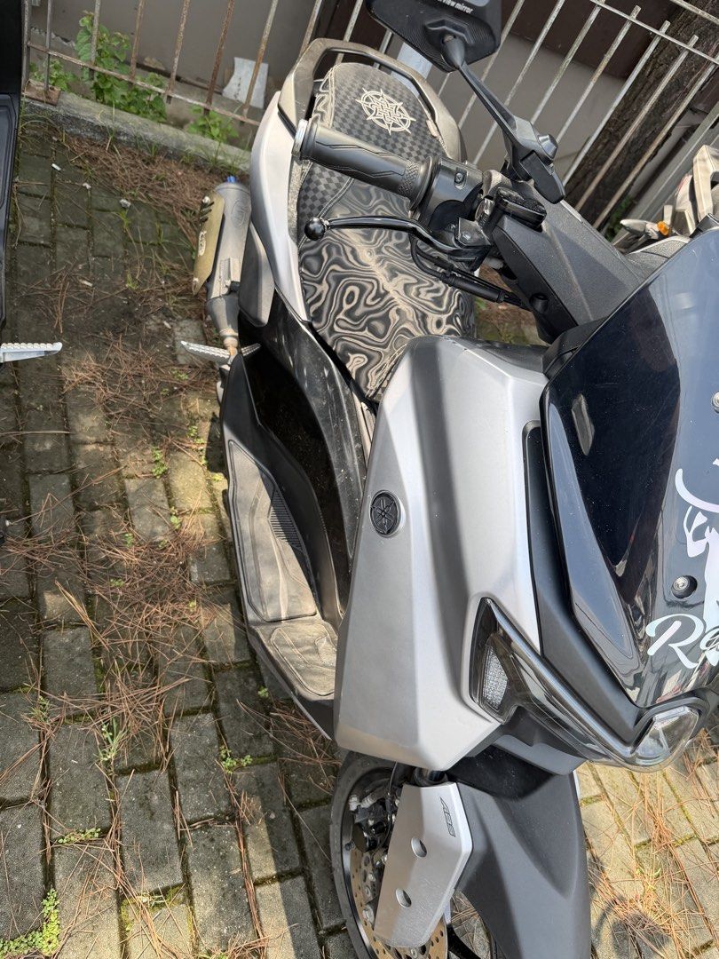 Yamaha NMAX v3 standard (Category: Motorbikes for Sale) located in Manila. Submitted by ballenwilm84291 (Listing ID 1467160018, Image 2). Description: Yamaha NMAX scooter finished in silver and black. Custom patterned seat with a compass-style emblem on top. JVT exhaust pipe installed with a blue tip. Windshield features playing card stickers and a Relax graphic. Dual rearview mirrors attached. Footboards and side panels show normal wear from dai