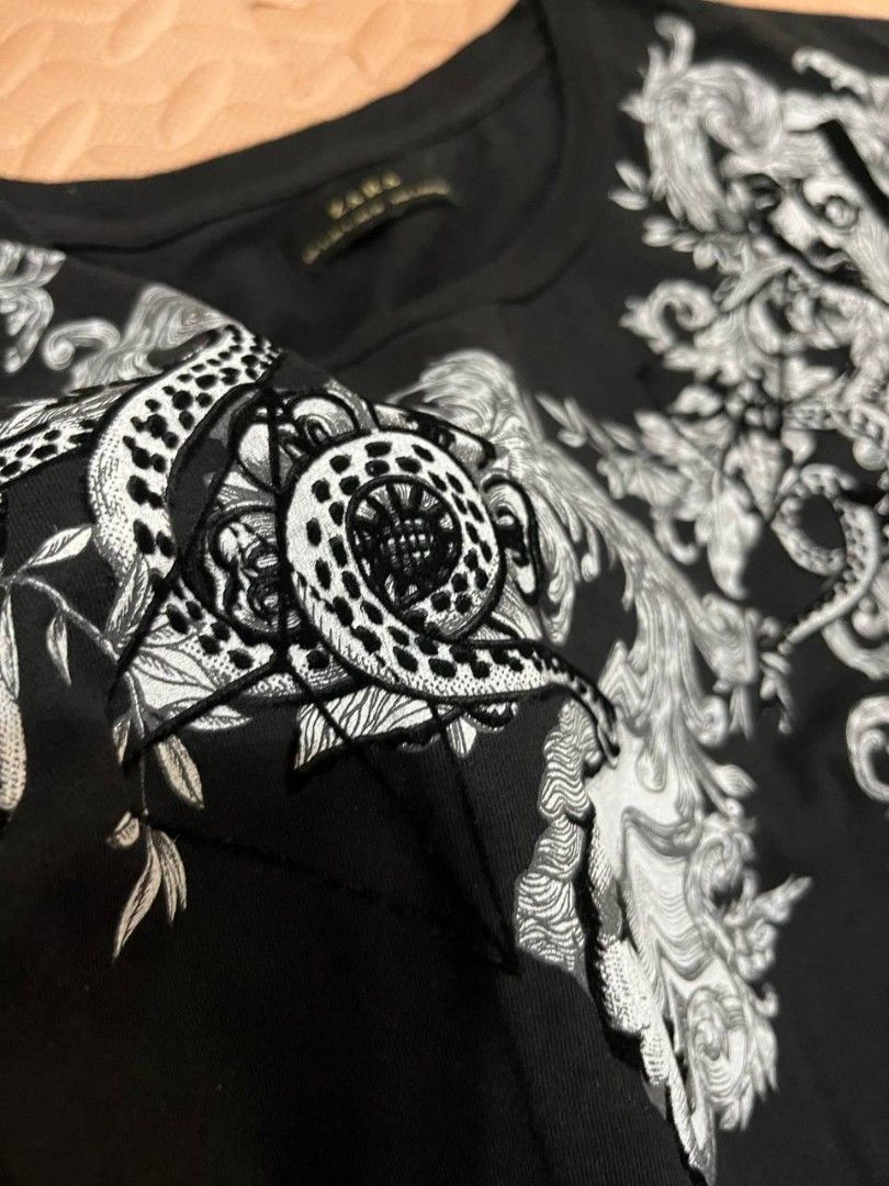 Zara Black Barocco Graphic Print Tee Size Small (Category: Shirts) located in Mandaluyong City. Submitted by soulanaa (Listing ID 1466985433, Image 2). Description: - Length: 28" - Bust: 18" - Shoulders: 17" - with velvet material on details Black t-shirt from Zara. Statement graphic print across the chest and shoulders featuring baroque scrollwork, classical faces, and snakes. Size S based on the collar tag. Cotton material, standard short sleev