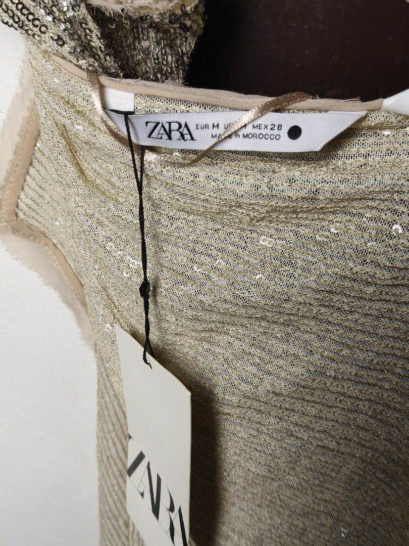 Zara Sequined Gold Halter Top (Category: Sleeveless) located in Manila. Submitted by ashie_clothing (Listing ID 1467164192, Image 3). Description: - Brand: Zara - Condition: Brand new with tags (BNWT), unworn - Size: Medium (true to size) - Color: Gold with heavy sequin detailing - Design: Halter neck, delicate spaghetti straps, and trendy asymmetrical hem - Material: Textured fabric base with full sequin overlay - Origin: Made in Morocco.