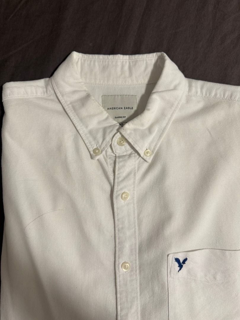 American Eagle Classic Fit White Button-Down Shirt Size L (Category: Tshirts & Polo Shirts ) located in Las Pinas. Submitted by luisanthonydelacruz (Listing ID 1467311057, Image 3). Description: American Eagle white button-down shirt in size Large. Features a classic fit, button-down collar, single chest pocket with embroidered eagle logo, and long sleeves. A versatile, clean wardrobe staple for any occasion..