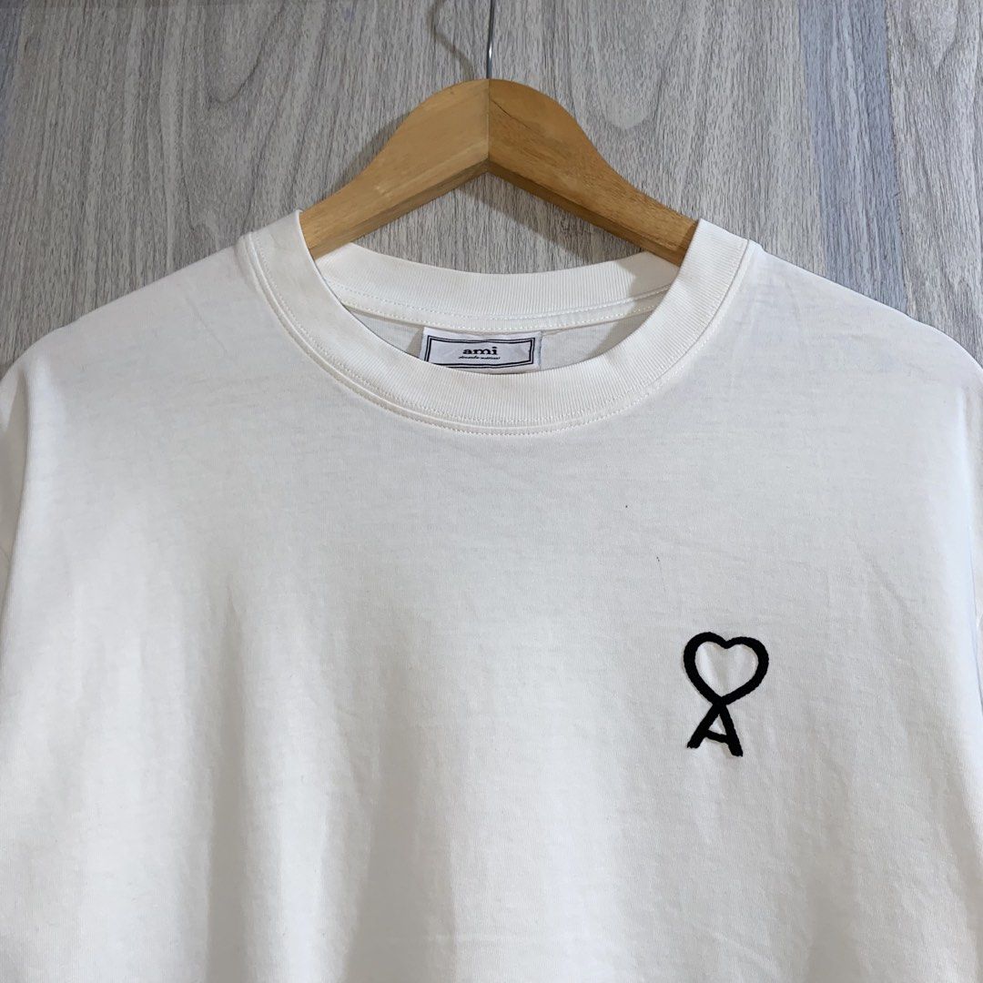 Ami Paris White Heart T-Shirt (Category: Shirts) located in Manila. Submitted by _thriftanddrip (Listing ID 1467276921, Image 2). Description: 22 x 27 Like new ₱700 White t-shirt from Ami Paris. Short sleeves with a ribbed crewneck collar. Features the signature black Ami de Coeur embroidered logo on the chest. Soft cotton fabric, clean styling. Regular fit, easy to match with daily outfits..