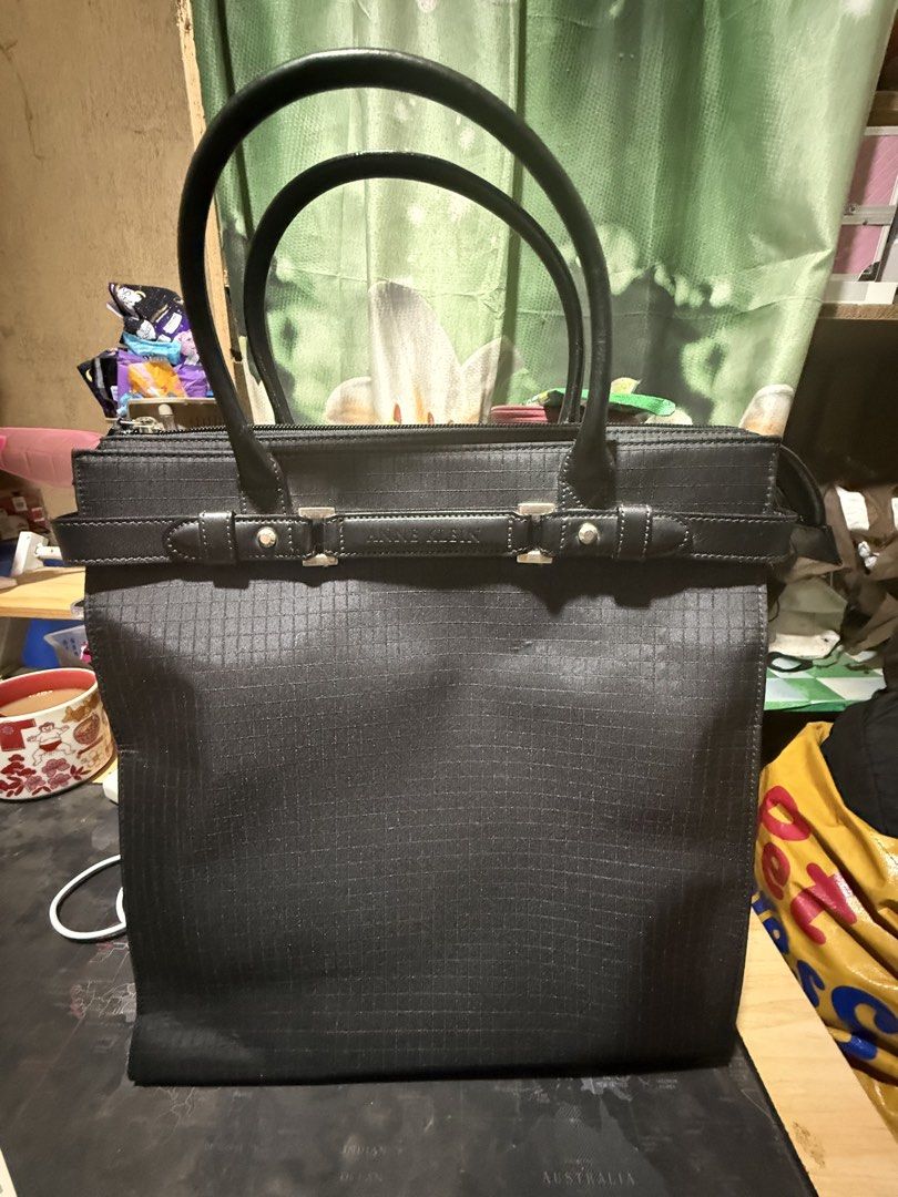 Anne Klein Black Tote Bag (Category: Tote Bags) located in Opol. Submitted by great_finds_kollexion (Listing ID 1467171733, Image 1). Description: Black structured tote bag by Anne Klein. Grid texture pattern on fabric exterior. Double handles with some wear along the edges visible in photos. Horizontal decorative strap across the front featuring the brand name embossed on metal-accented hardware. Exterior back pocket with zipper closure. Fabric 