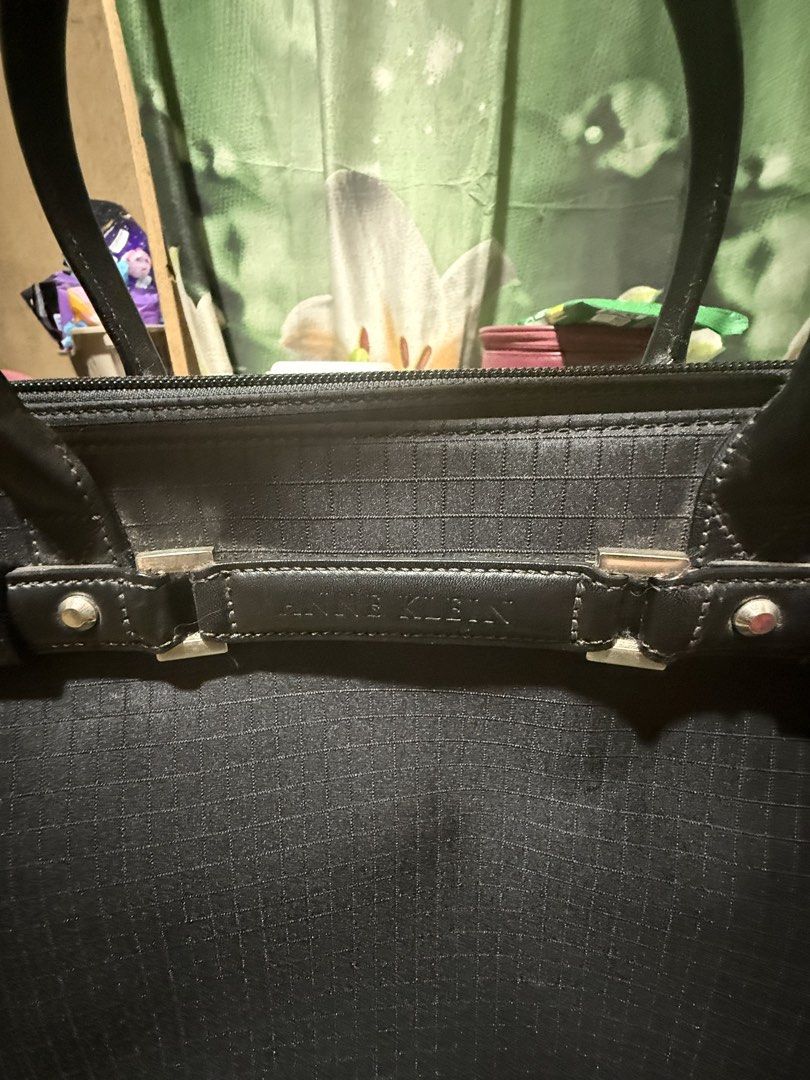 Anne Klein Black Tote Bag (Category: Tote Bags) located in Opol. Submitted by great_finds_kollexion (Listing ID 1467171733, Image 3). Description: Black structured tote bag by Anne Klein. Grid texture pattern on fabric exterior. Double handles with some wear along the edges visible in photos. Horizontal decorative strap across the front featuring the brand name embossed on metal-accented hardware. Exterior back pocket with zipper closure. Fabric 