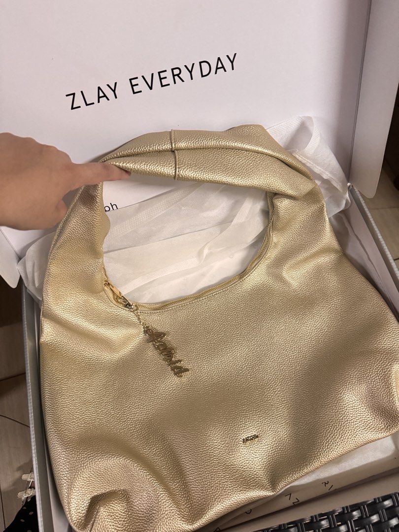 Astrid Metallic Gold Shoulder Bag (Category: Luxury Bags & Wallets) located in Muntinlupa City. Submitted by mimitatsboutique (Listing ID 1467307897, Image 1). Description: - Color/Finish: Chic gold textured faux leather - Closure: Zip top with a stylish matching charm - Interior: White fabric lining with a convenient zipped side pocket - Packaging: Includes original white box.