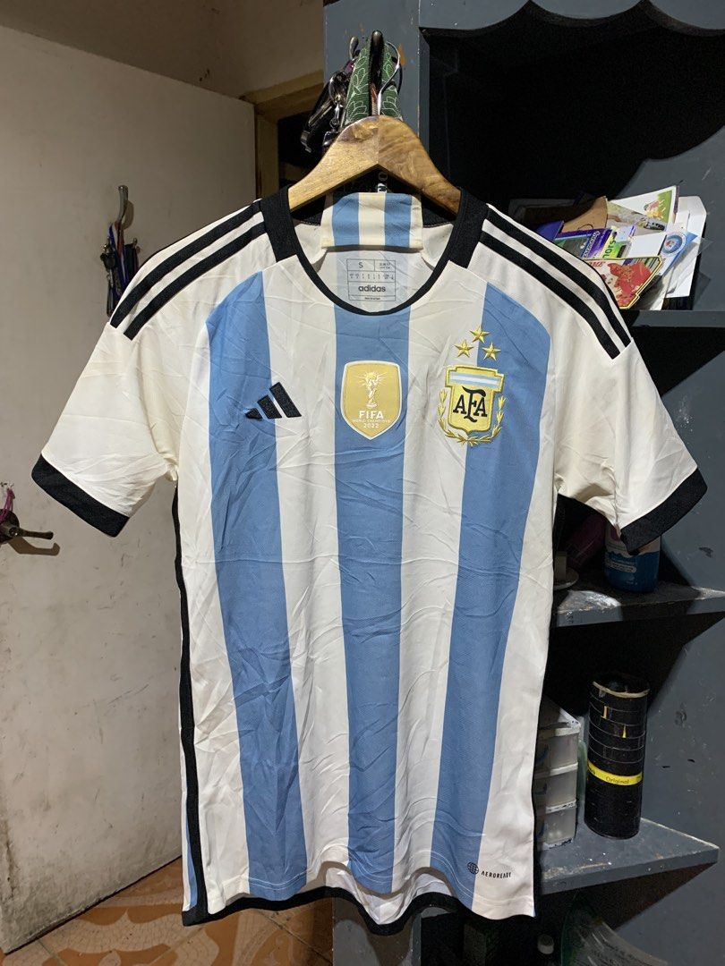 Authentic Argentina 22 Messi Jersey Winners Home (Category: Tshirts & Polo Shirts ) located in Bulacan. Submitted by aaron_garrucho15 (Listing ID 1467344721, Image 1). Description: Medium best fit (small on tag) - Item: Argentina 2022 World Cup Home Jersey - Size: S (Slim Fit) - Design: White and light blue stripes with black accents - Details: Embroidered AFA crest, 3 stars, and Adidas logo - Special Feature: Gold FIFA World Champions 2022 badge