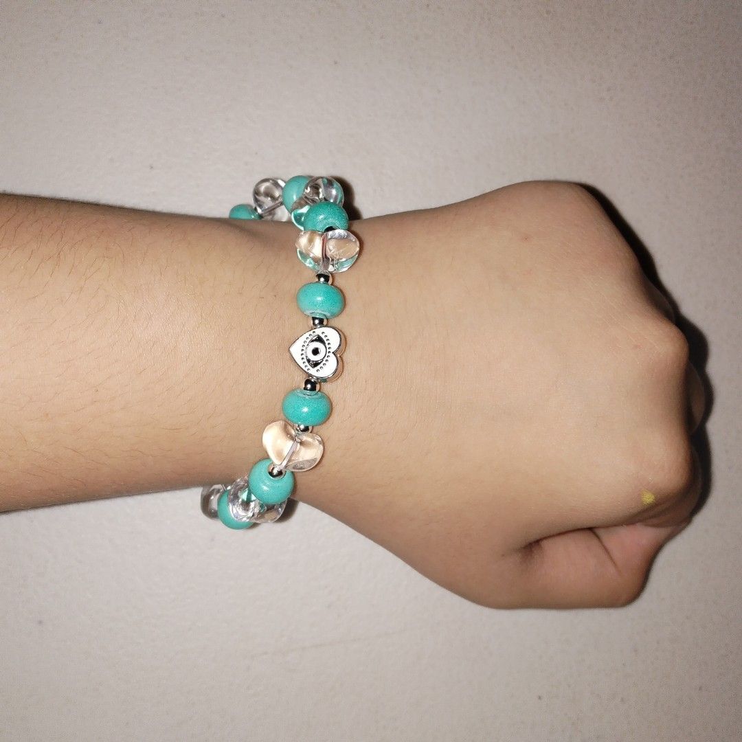 Beaded bracelet with turquoise beads and evil eye charm (Category: Bracelets) located in Makati City. Submitted by clover_2024 (Listing ID 1467353589, Image 2). Description: - Handmade beaded bracelet - Turquoise round beads & clear heart-shaped glass beads - Silver-tone metal spacer beads - Central white heart charm with black evil eye symbol - Stretchy elastic cord fits most wrists - Cute everyday accessory for casual outfits.