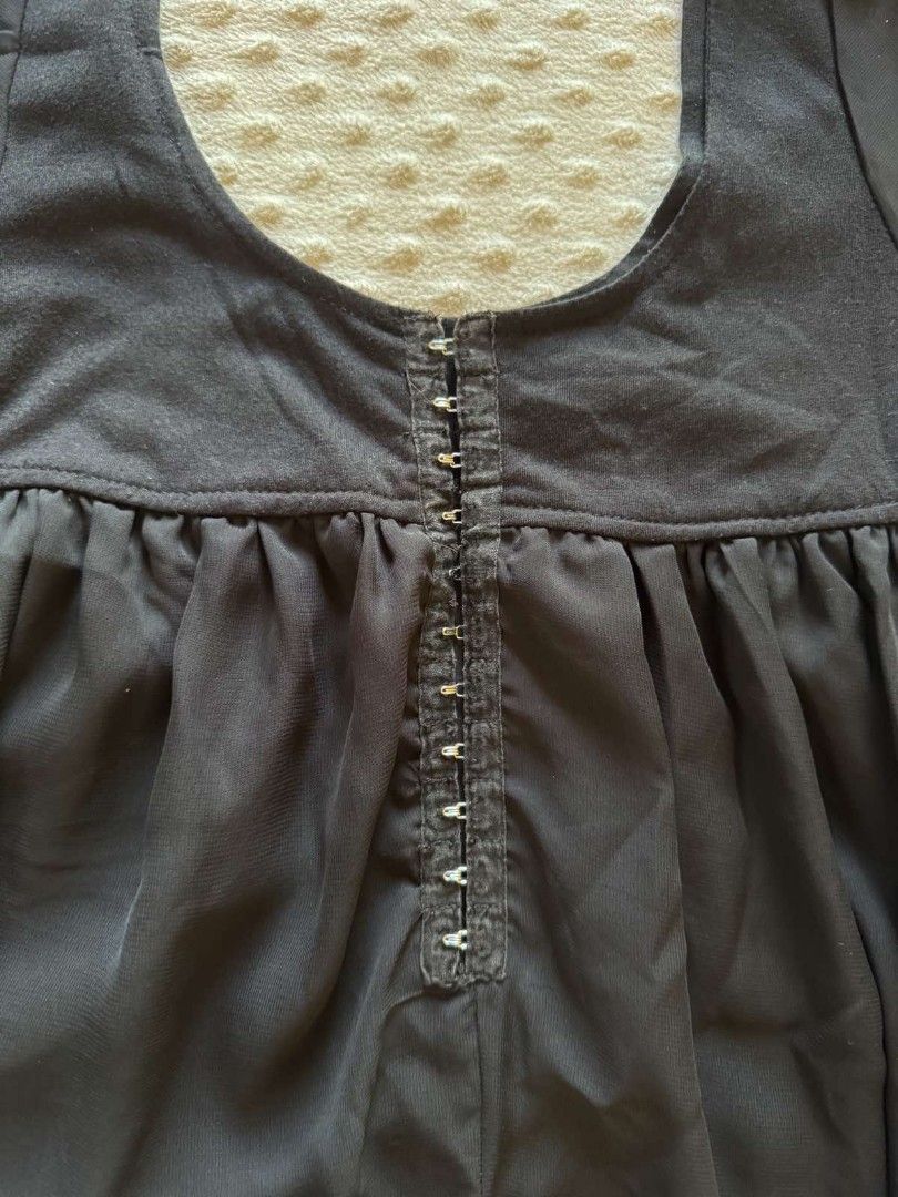 Black blouse with front hook closure and sheer chiffon hem (Category: Blouses) located in Calamba. Submitted by iam.hides (Listing ID 1467206091, Image 3). Description: - Color: Black - Style: Short-sleeve top with scoop neckline and sheer sleeve accents - Closure: Functional metal hook-and-eye closure down the center front - Design: Fitted bodice with a gathered, flowy chiffon skirt layer - Material: Soft cotton blend upper - Length: Approximate
