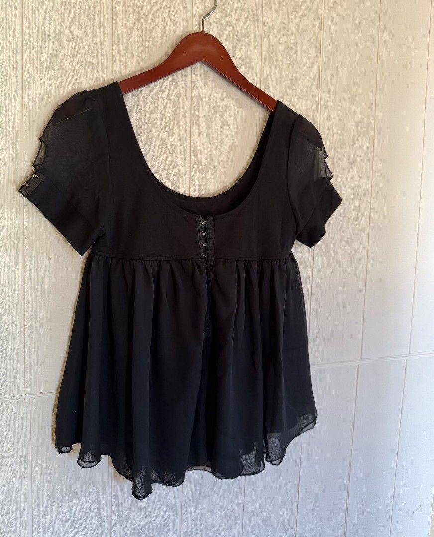 Black blouse with front hook closure and sheer chiffon hem (Category: Blouses) located in Calamba. Submitted by iam.hides (Listing ID 1467206091, Image 2). Description: - Color: Black - Style: Short-sleeve top with scoop neckline and sheer sleeve accents - Closure: Functional metal hook-and-eye closure down the center front - Design: Fitted bodice with a gathered, flowy chiffon skirt layer - Material: Soft cotton blend upper - Length: Approximate