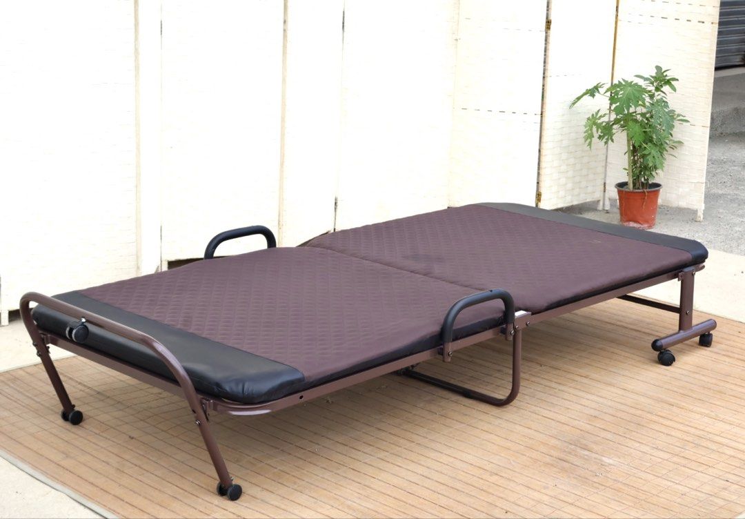 Brown Folding Bed with Wheels and Quilted Mattress (Category: Bed Frames & Mattresses) located in Bulacan. Submitted by FurnitureGallery (Listing ID 1467309515, Image 2). Description: - Type: Folding single bed - Color: Brown frame with black padded ends - Comfort: Built-in quilted mattress - Mobility: Equipped with wheels and side safety handles - Storage: Folds completely in half for compact storage - Ideal for: Small apartments, dorms, or gues