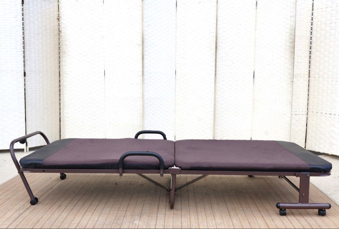Brown Folding Bed with Wheels and Quilted Mattress (Category: Bed Frames & Mattresses) located in Bulacan. Submitted by FurnitureGallery (Listing ID 1467309515, Image 1). Description: - Type: Folding single bed - Color: Brown frame with black padded ends - Comfort: Built-in quilted mattress - Mobility: Equipped with wheels and side safety handles - Storage: Folds completely in half for compact storage - Ideal for: Small apartments, dorms, or gues