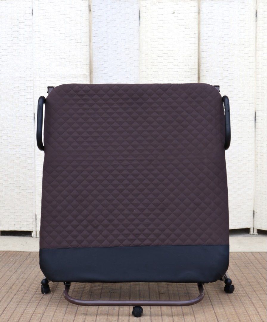 Brown Folding Bed with Wheels and Quilted Mattress (Category: Bed Frames & Mattresses) located in Bulacan. Submitted by FurnitureGallery (Listing ID 1467309515, Image 3). Description: - Type: Folding single bed - Color: Brown frame with black padded ends - Comfort: Built-in quilted mattress - Mobility: Equipped with wheels and side safety handles - Storage: Folds completely in half for compact storage - Ideal for: Small apartments, dorms, or gues