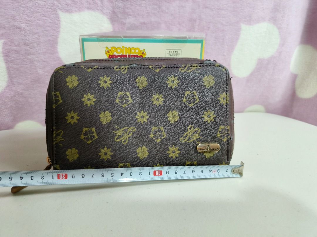 Brown pattern zippered wallet (Category: Wallets & Card holders) located in San Leonardo. Submitted by burgossanleonardo.12345 (Listing ID 1467278821, Image 2). Description: - Material: Brown faux leather with gold-toned monogram pattern (clover and star motifs) - Closure: Secure zip-around with light brown pull tab - Features: Small metallic logo plaque on front, convenient back slip pocket - Condition: Compact size with visible edge peeling and