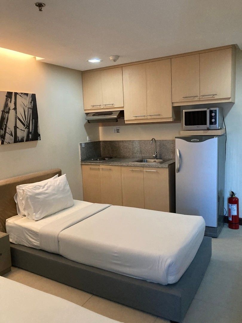 BSA Twin Tower Condominium (Category: Apartments & Condos) located in Muntinlupa City. Submitted by lazoftoys (Listing ID 1467256002, Image 2). Description: - Twin bed studio unit, ready to move in - Private bathroom with glass shower enclosure - Built-in kitchenette with microwave and refrigerator - TV setup and air conditioning installed - Ample overhead storage cabinets and wardrobe space - Sleek, modern, and well-maintained finish.