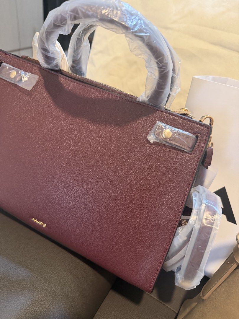 Burgundy Structured Handbag with Gold Hardware and Strap (Category: Luxury Bags & Wallets) located in Manila. Submitted by bella.yuno (Listing ID 1467305741, Image 2). Description: - Color: Burgundy - Material: Premium textured leather with gold-tone hardware - Condition: Brand new with protective plastic still wrapped on dual top handles and side hardware - Straps: Includes dual top handles and a removable shoulder strap (still wrapped) - Design