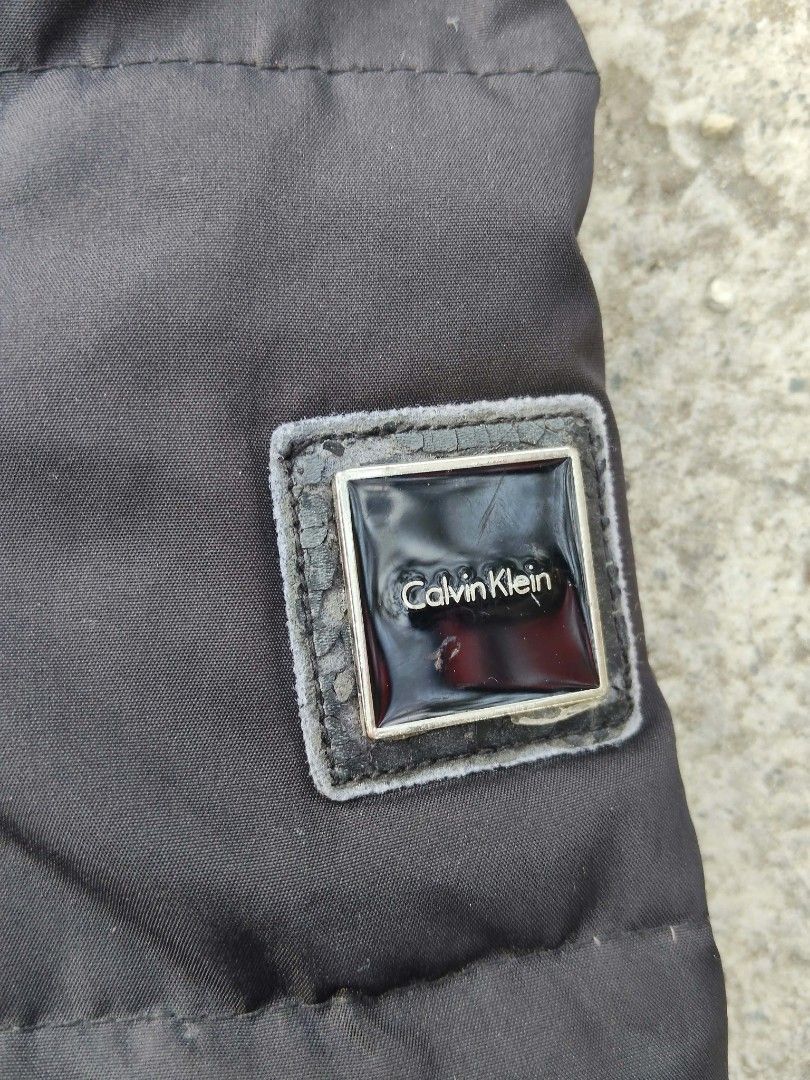 Calvin Klein Black Puffer Jacket with Hood (Category: Coats, Jackets and Outerwear) located in Lucena. Submitted by ziboldawg (Listing ID 1467346646, Image 3). Description: - Brand: Authentic Calvin Klein - Color: Classic Black - Size: Small - Design: Quilted puffer with built-in hood - Pockets: Zippered side pockets for security - Details: Branded metal zipper hardware and glossy logo patch on the left sleeve - Condition: Clean, well-kept, and w