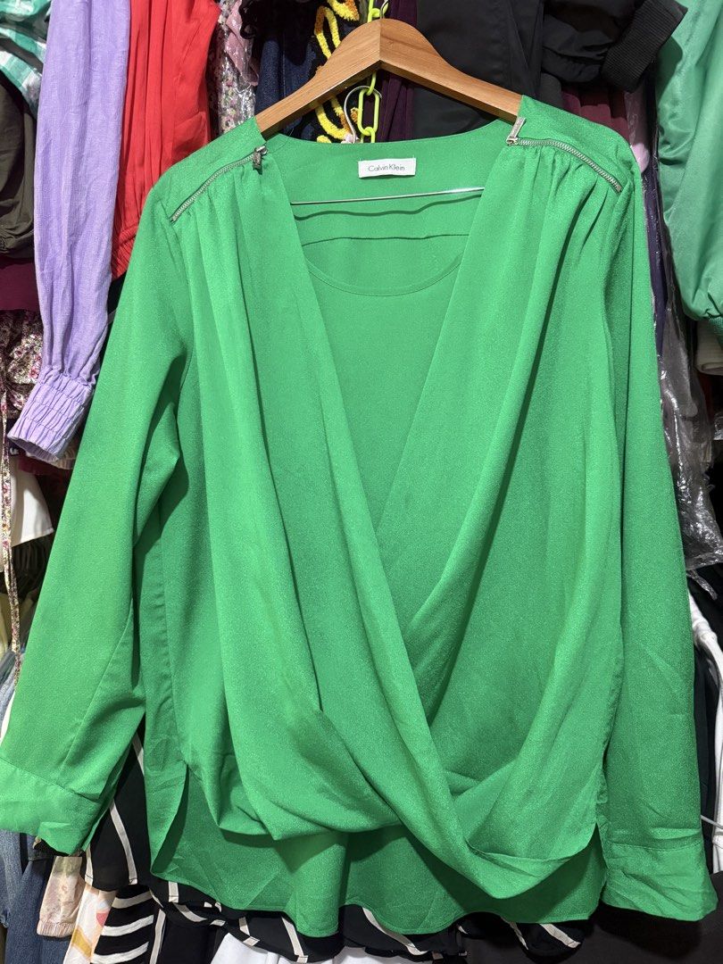 Calvin Klein Green Wrap Blouse (Category: Blouses) located in Antipolo. Submitted by harlowwillow (Listing ID 1467173551, Image 1). Description: 🙅‍♀️NO TO LOW BALLERS No size on tag W L - Color: Bright green - with green inner like - Style: Wrapped front design with zipper hardware on both shoulders - Sleeves: Long sleeves with button cuffs and can be folded - Fabric: Soft drape, comfortable fit - Condition: Good, with tiny dark ink mark on the 