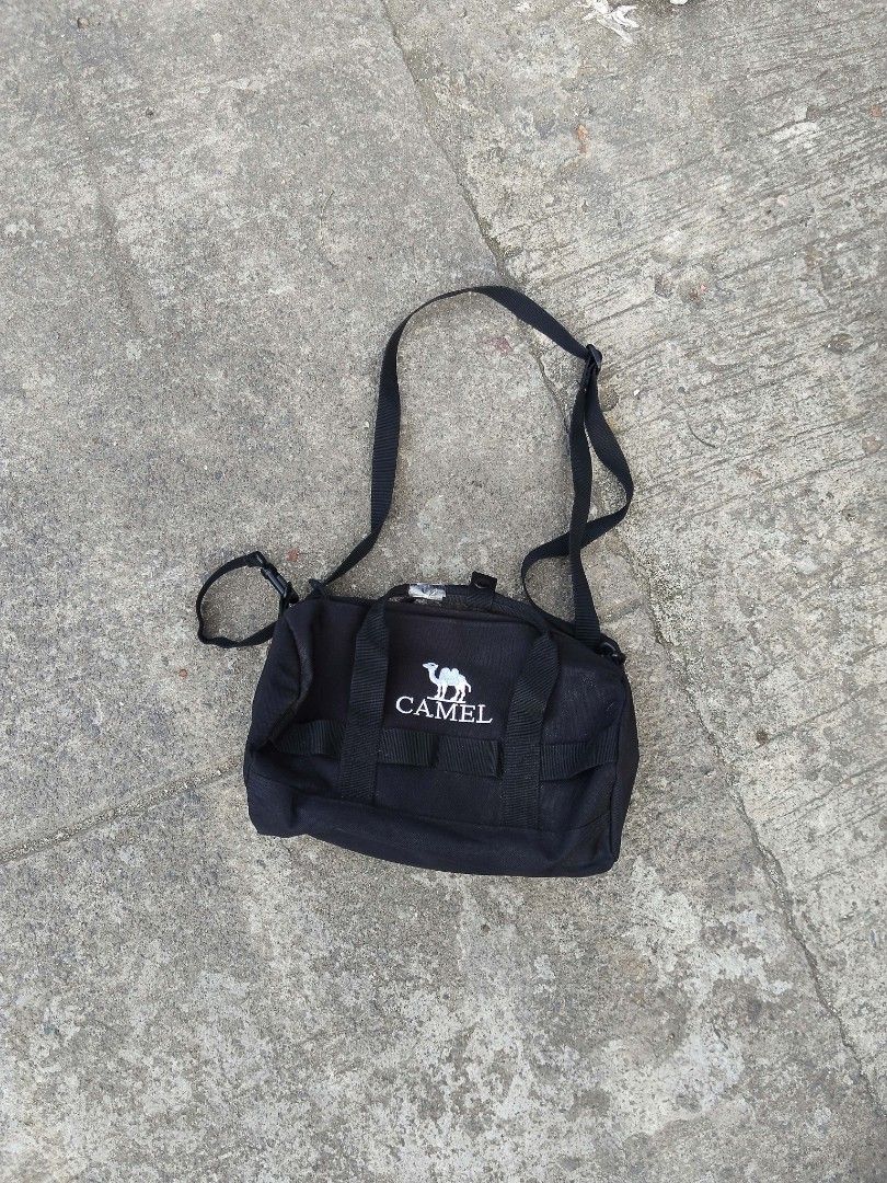 Camel Black Crossbody Duffel Bag (Category: Cross-body Bags) located in Lucena. Submitted by ziboldawg (Listing ID 1467347029, Image 3). Description: Black Camel duffel crossbody bag. Small size, measuring roughly 270mm. Dual top grab handles plus an adjustable shoulder strap. White Camel logo printed prominently on the front. Durable fabric construction with interior tag labels intact. Great compact shape for daily outings, gym trips, or quick t